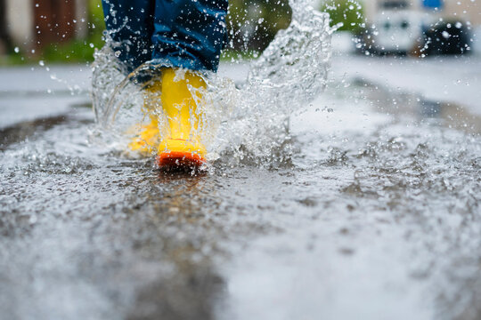 Child in yellow boots splashing in a puddle outdoors