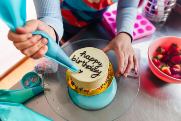 Young woman piping happy birthday using icing bag on cake