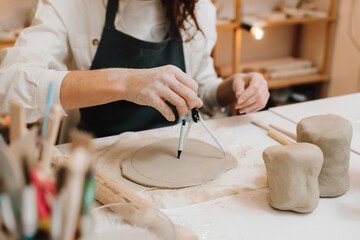 Artisan with compass shapes and refines a ceramic piece with precision. Potter works on a clay slab...