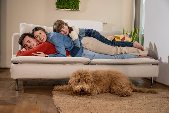 Happy family relaxing on sofa near dog at home