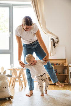 Cheerful baby girl learning to walk with mother at home