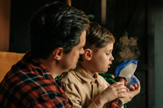 Father helping son use an inhaler at home for cold treatment