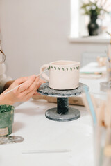 Process of designing cup with a traditional pattern in pottery art studio. Artisan stamps decorative symbols on the dry clay of the cup.