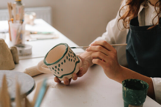 Experienced artist painting designs on ceramic cup in pottery workshop. Potter draws an abstract design into earthenware cup.