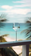 A water glass standing tall on a balcony railing overlooking a serene beach view