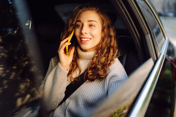 Relaxing moment of beautiful woman sitting in car back seats using smartphone. Concept of...