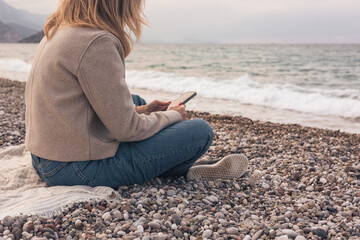 Pretty woman using her phone, while sitting on the beach