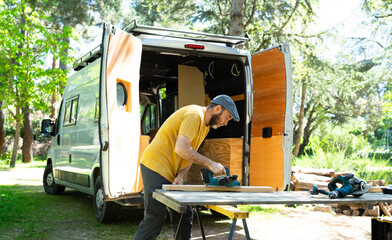 Carpenter working on wood plank near camper van in forest