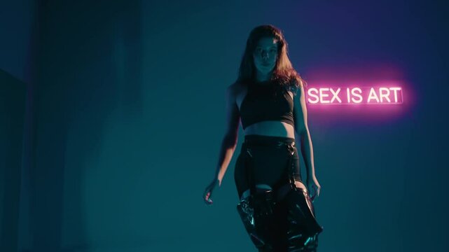 A young woman dances seductively in a dimly lit room with a neon sign. The neon sign adds a provocative touch, creating a captivating atmosphere. Sensual Dance Performance