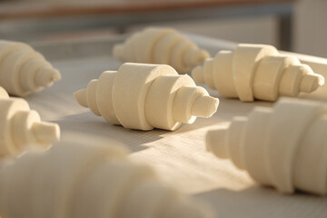 Freshly shaped pastry rolls lie on a wooden surface in a cozy bakery, ready for baking in early...