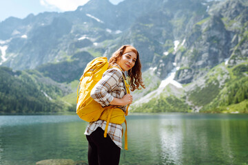 Beautiful Caucasian female hiker with backpack standing near beautiful lake. Active life. Travel,...
