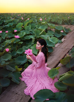 Beautiful young asian woman on lotus lake at sunset.