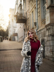 Fototapeta premium Beautiful blonde Slavic woman in a fur coat walks along the old streets.