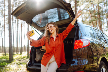 Young woman is resting in trunk of car and taking selfie. Blogging, communication, technology....