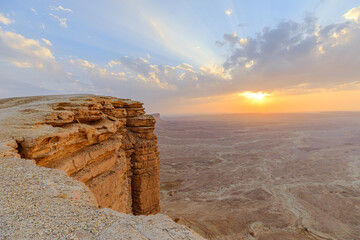 Golden hour sunlight illuminates the Tuwaiq escarpment at sunset, casting long shadows across the desert landscape near Riyadh, Saudi Arabia, a breathtaking view from the edge of the world