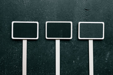 Three blank wooden chalkboard plant labels on a dark textured background. Minimalist gardening markers for organizing herbs, vegetables, and flowers. Space for customizable text or names