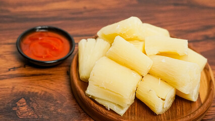 boiled cassava served on a wooden background. with spicy red chili sauce
