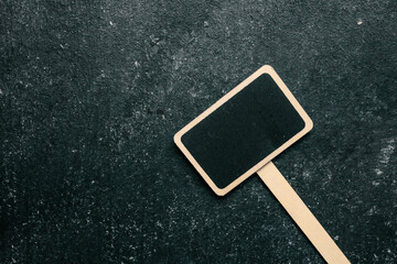 Blank mini chalkboard sign with a wooden stick on a dark textured background. Ideal for labeling...