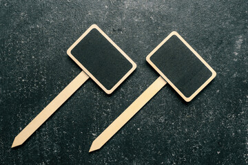 Two blank mini chalkboard signs with wooden stakes on a dark textured background. Perfect for labeling plants, garden markers, or decorative signs
