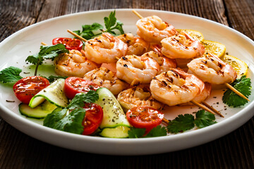 Grilled skewer shrimps and fresh vegetables on wooden table	