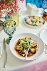 There is a plate of food, a spoon and a knife on the table. The dish consists of eggplant vegetable rolls with sauce.