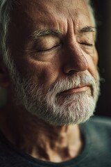Fototapeta premium Bearded man with graying hair and mustache, eyes closed, head tilted slightly upwards in meditation pose.