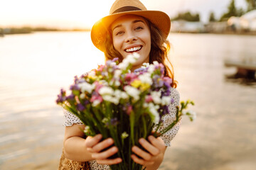 Happy young girl in a white dress with a bouquet of wild flowers walks in the sunset.  Rustic style...