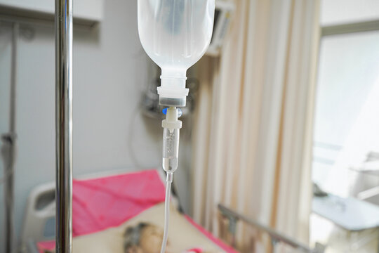 Close-up of intravenous saline  infusion set for patient with blurred patient background in hospital. IV drip in the patient ward, Medical and health concepts