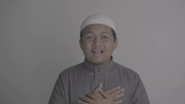 Southeast Asian Muslim man wearing grey robe makes greeting gesture, then chats amiably with people around him