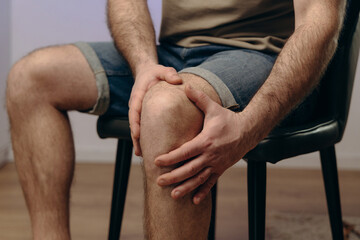 man holding his knee in pain. hands are tightly gripping affected area, there is tension in his...