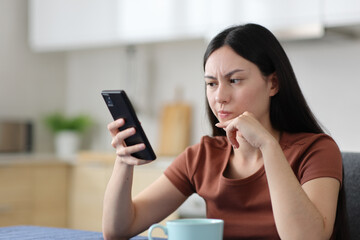 Suspicious asian woman checking phone in the kitchen