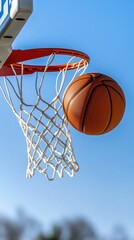 Fototapeta premium A basketball gracefully swishes through the net as players enjoy an exhilarating outdoor game beneath a clear blue sky