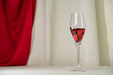 Wine glass with heart confetti on cream and red silk background. Minimalist holiday photo for Valentines
