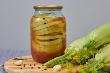 a jar of zucchini in marinade, canned zucchini in a jar and fresh zucchini on a wooden board on the...