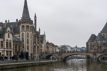 Fototapeta premium Medieval gothic buildings and a stone arch bridge line the historic canal on a gray winter day in Ghent Belgium