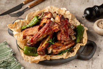Oven baked pork ribs with garlic, rosemary, honey, ketchup and garlic, baked green bell peppers. Beige, brown table surface.