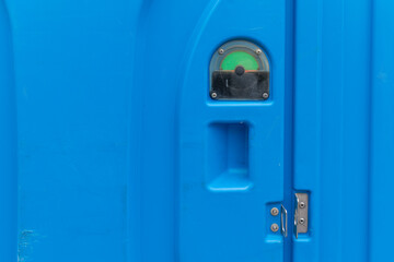 Bright blue portable restroom shows green indicator, signaling availability, at an outdoor event during daylight hours