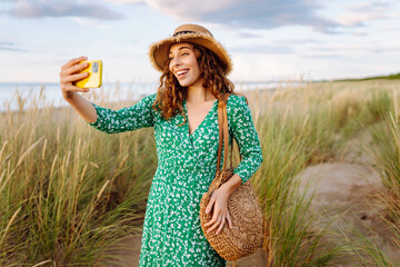 Young woman walking to the sea along the tall grass takes a selfie on her phone. Summer walks....