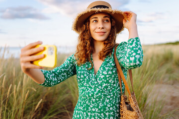 Young woman walking to the sea along the tall grass takes a selfie on her phone. Summer walks....