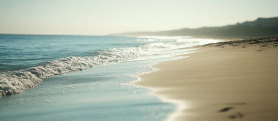 Obraz premium Soft waves lapping a tranquil sandy beach at sunrise.