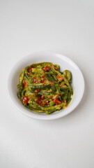 A portion of Balinese jukut bejek mixed with sambal embe made from long beans is served in a white plate placed with a white background (isolated white).