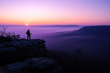 Silhouetted hiker enjoys sunrise over misty valley.
