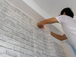  Man hand are putting up wallpapers on the wall in the room which renovation his home.