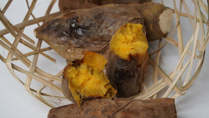 Cilembu roasted sweet potatoes in a bamboo basket are placed on a white base and background (isolated white).