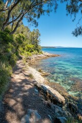 Coastal walking trail alongside crystal-clear turquoise water, rocky shoreline, and lush green vegetation under a sunny blue sky.