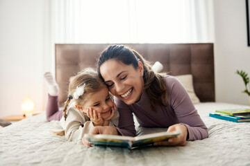 Portrait of happy mother reading a story form a book to her adorable little daughter.