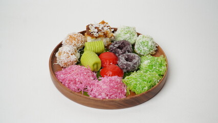 Various market snacks consisting of klepon, awug, jalabria, getuk, putu mayang and cikak are served on a wooden plate lined with banana leaves placed on a white base and background (isolated white).