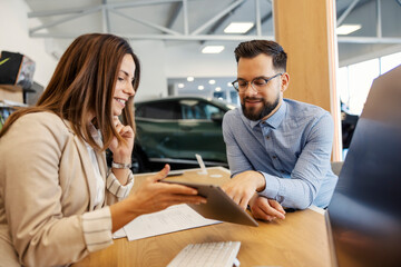 Car dealer and customer sitting in office at car salon and filling up forms on tablet.