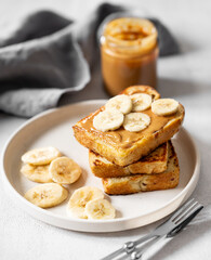 Peanut butter toast with banana on a plate on a light background with jar and  napkin close up.