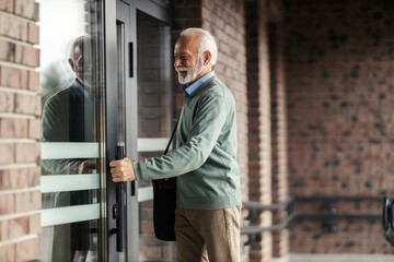 A smiling stylish senior man entering a building.